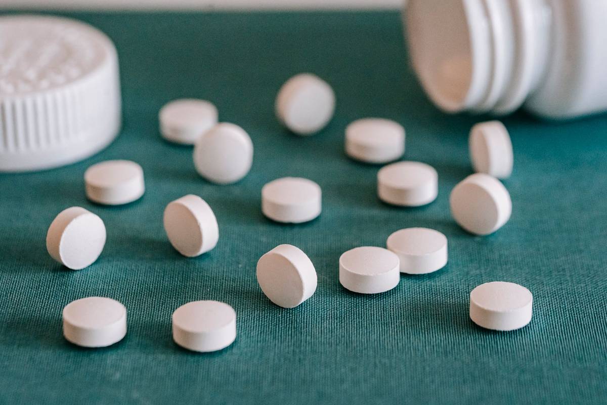 Closeup of assorted similar white round pills spilled from plastic bottle on green surface