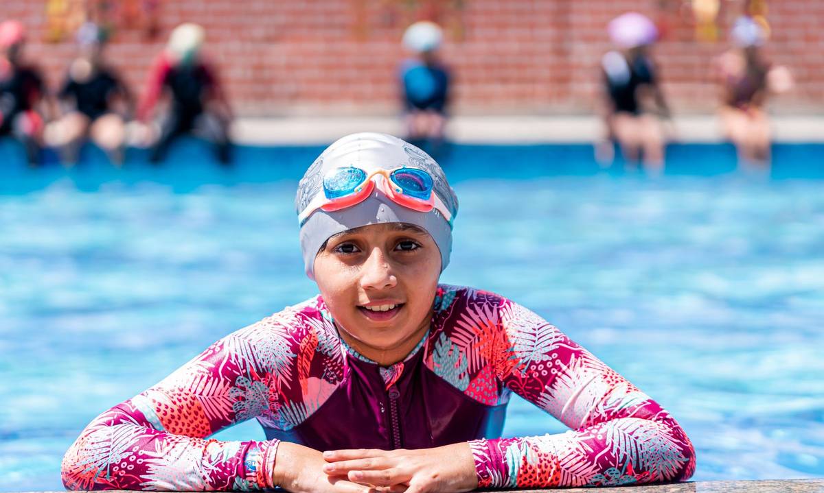 A young swimmer enjoys a sunny day at the outdoor pool, wearing a colorful swimsuit and goggles.